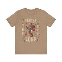 Praise the Lord Tee features a festive cross in patchwork style, surrounded by snowflake motifs, with PRAISE THE LORD and Psalms 106:1 framing it.