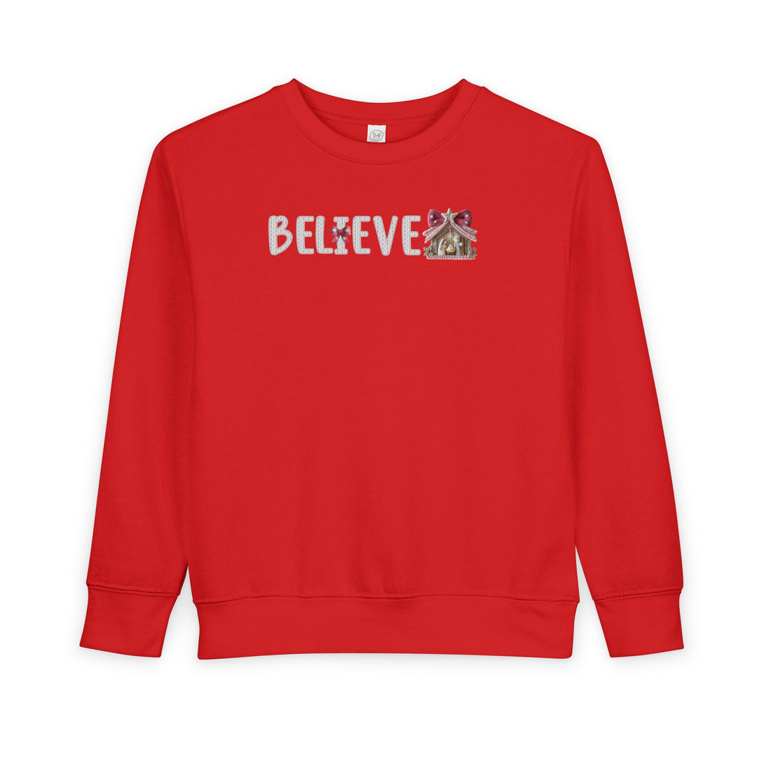 Toddler crew-neck sweatshirt with BELIEVE design featuring a Christmas ornament as I and a nativity scene as E, blending comfort with festive style.