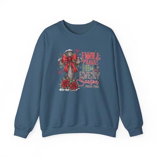Slate-blue crewneck sweatshirt featuring a rustic wooden cross with a red bow, surrounded by snowflakes, poinsettias, and the phrase “I WILL PRAISE HIM in EVERY Season.”