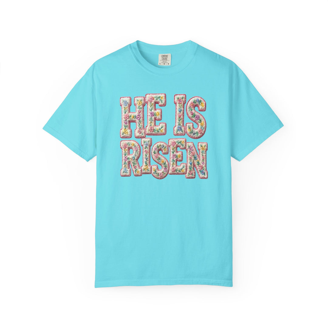 He is Risen Tee with pastel floral motif letters on light-blue fabric, showcasing Comfort Colors tag. Available in various sizes, offering luxurious comfort and style.