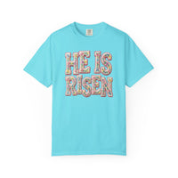 He is Risen Tee with pastel floral motif letters on light-blue fabric, showcasing Comfort Colors tag. Available in various sizes, offering luxurious comfort and style.