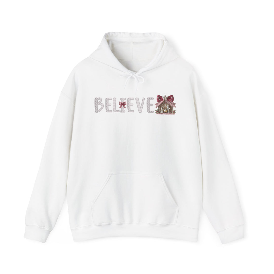 White Believe hoodie with a knit-style font, red bow detail, and nativity-stable graphic. Features a kangaroo pocket and matching drawstring hood for warmth and style.