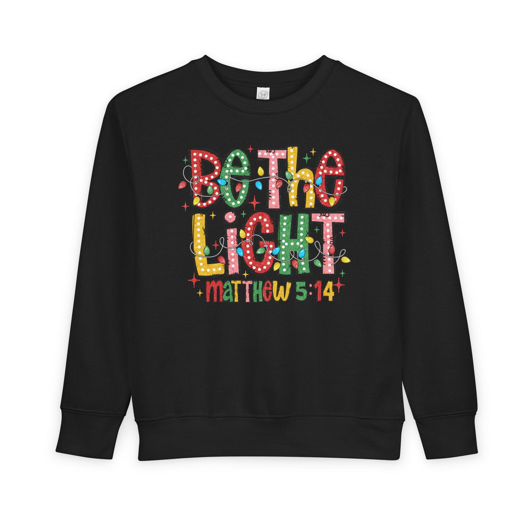 Be the Light Toddler Crew: Black sweatshirt with festive Be the Light graphic and Matthew 5:14, offering warmth and comfort with durable cotton-polyester blend.