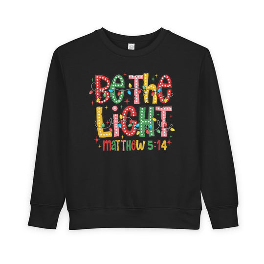 Be the Light Toddler Crew: Black sweatshirt with festive Be the Light graphic and Matthew 5:14, offering warmth and comfort with durable cotton-polyester blend.