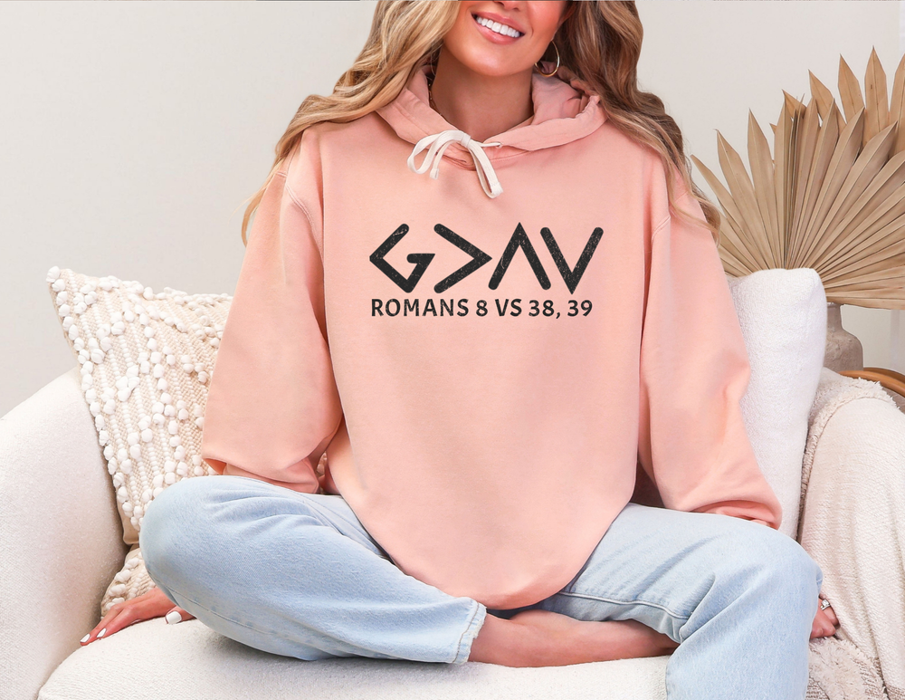 Woman sitting on a couch wearing the God is Greater Hoodie - Matching Set, showcasing its relaxed fit and jersey-lined hood crafted from 100% ring-spun US cotton.