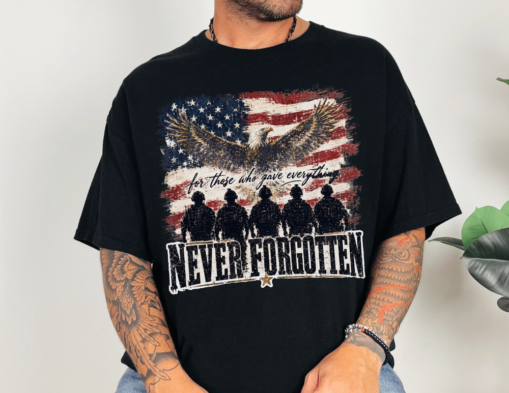 Person wearing the Never Forgotten Tee featuring a memorial graphic with an eagle, distressed flag, and soldiers, highlighting the slogan “for those who gave everything.”