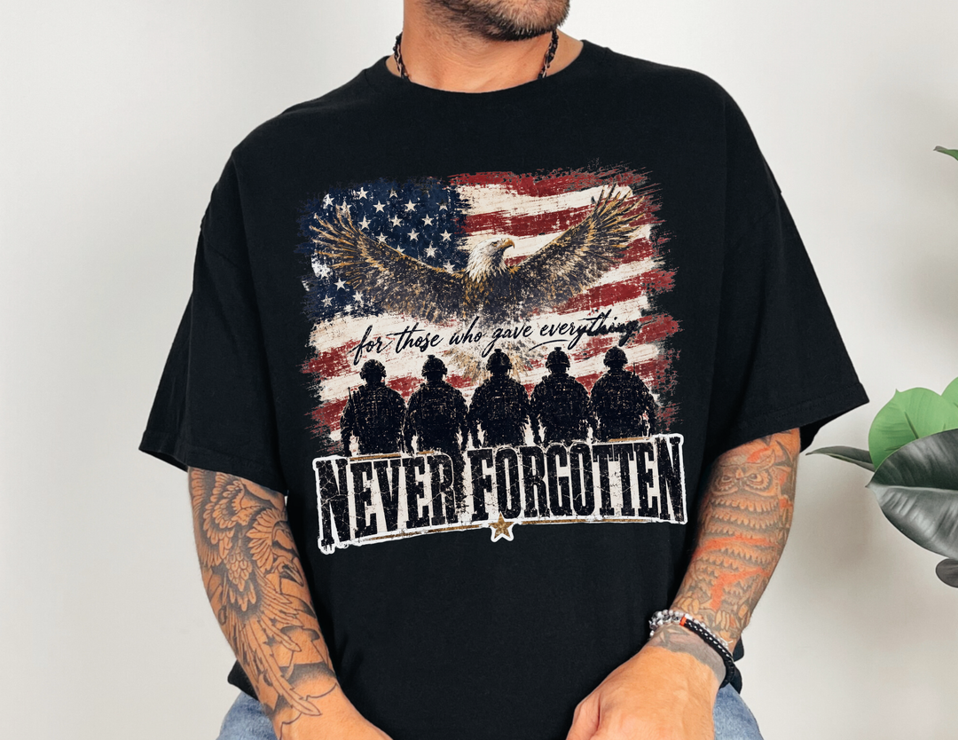 Person wearing the Never Forgotten Tee featuring a memorial graphic with an eagle, distressed flag, and soldiers, highlighting the slogan “for those who gave everything.”
