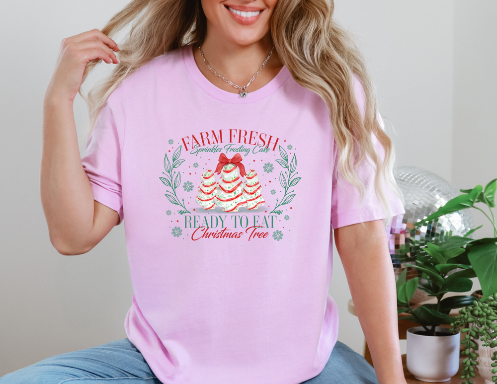 Farm Fresh Cookies Tee featuring a holiday-themed graphic with Christmas tree cakes, surrounded by festive foliage and snowflakes, worn by a person.