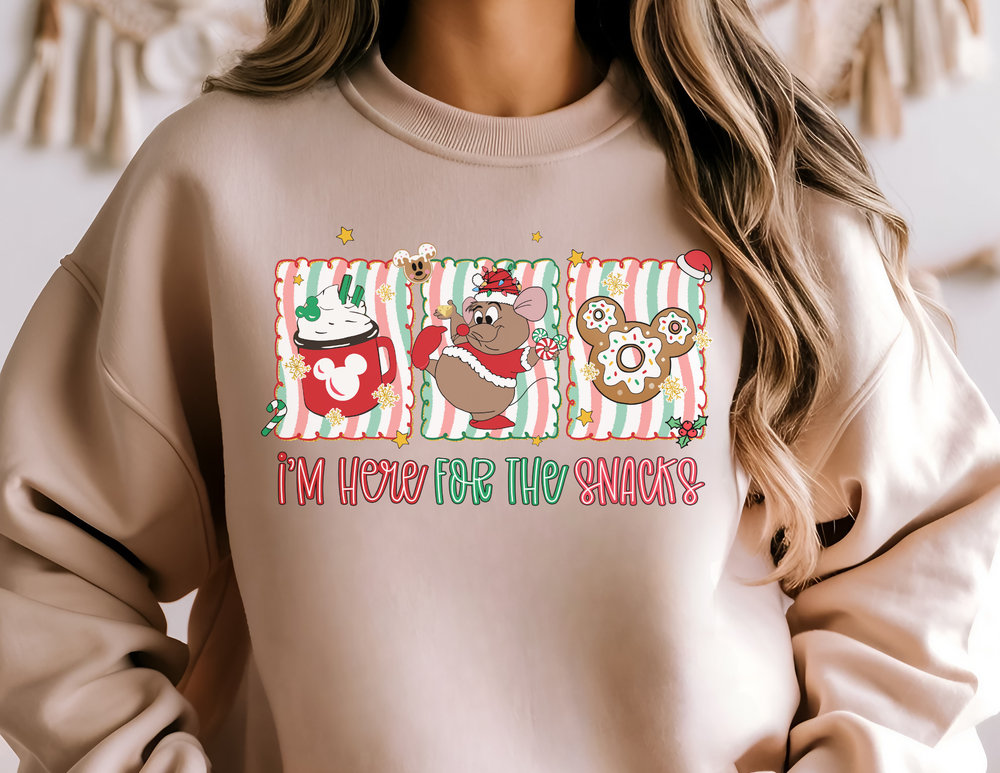 Light-beige sweatshirt with festive graphics: hot cocoa mug, Santa mouse, Mickey gingerbread, and 'I'M HERE FOR THE SNACKS' slogan, offering cozy comfort.