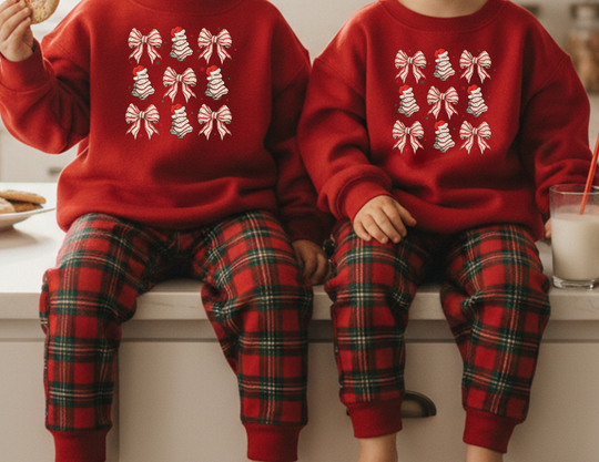 Toddlers wear matching Cookies and Bows Toddler Crew sweatshirts on a kitchen counter, one holding a cookie, showcasing cozy holiday-themed attire.