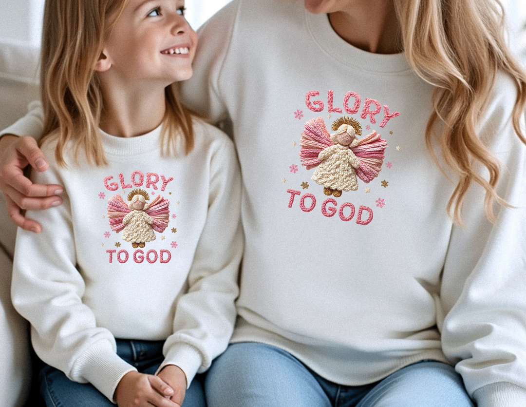 Woman and girl in matching Glory to God Toddler Crew sweatshirts with angel embroidery, smiling at each other, suggesting a warm, festive atmosphere.