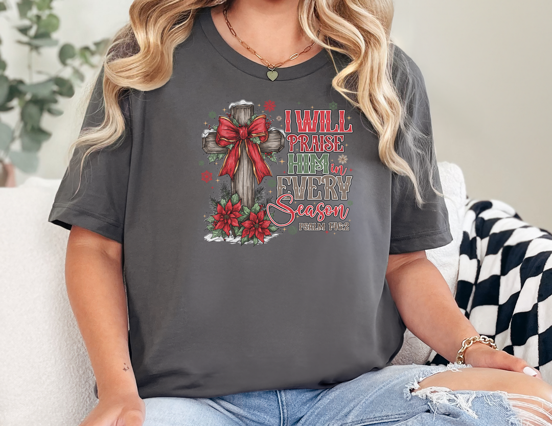 Praise Him in Every Season Tee displaying a festive wooden cross with a red bow, poinsettias, and scripture, ideal for holiday celebrations.