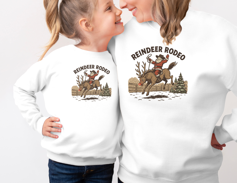 Two people in matching Reindeer Rodeo Crew sweatshirts featuring Santa in cowboy gear on a reindeer, capturing festive, vintage Western style.