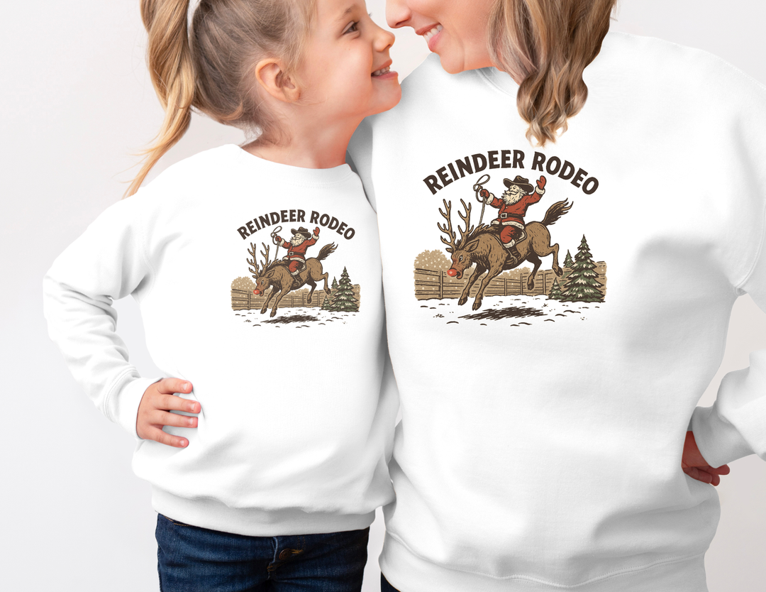 Two people in matching Reindeer Rodeo Crew sweatshirts featuring Santa in cowboy gear on a reindeer, capturing festive, vintage Western style.