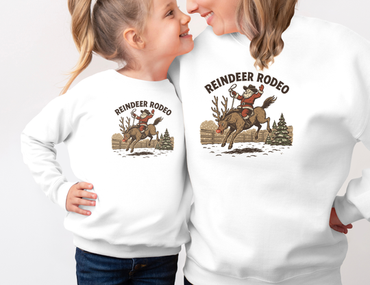Two people in matching Reindeer Rodeo Crew sweatshirts featuring Santa in cowboy gear on a reindeer, capturing festive, vintage Western style.
