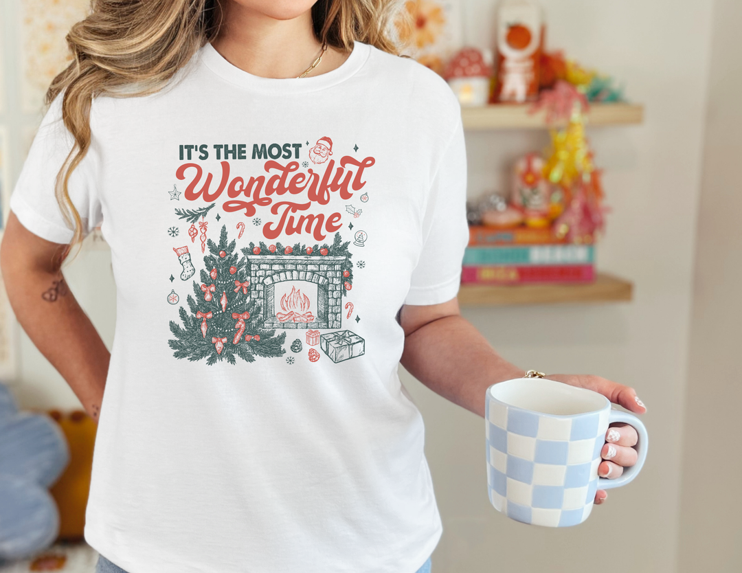 Person wearing Most Wonderful Time of the Year Tee with festive holiday design, holding a checkered mug; cozy seasonal vibe.