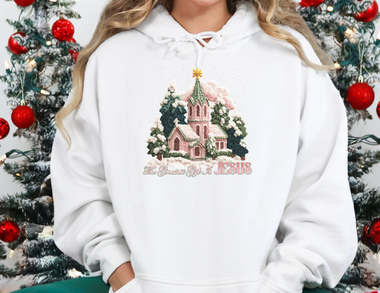 Person wearing the Gift is Jesus Hoodie, featuring a serene church scene with evergreens, star, and message, ideal for cozy, faith-inspired style.