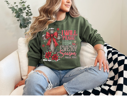 Woman wearing a Praise Him in Every Season Crew sweatshirt with festive cross design, seated on a chair, showcasing the comfortable, durable fit and seasonal theme.