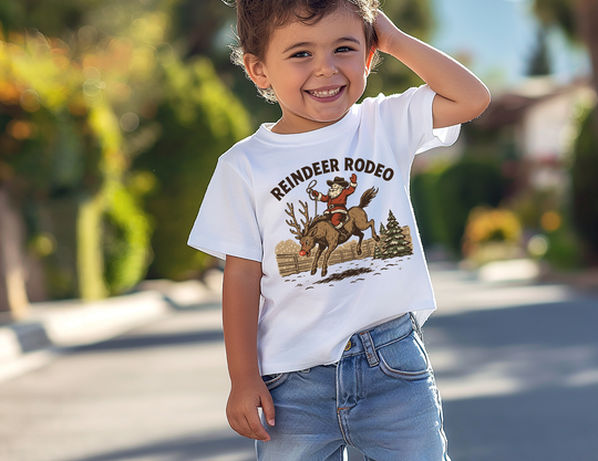 Toddler wearing Reindeer Rodeo Kids Tee with Santa on a reindeer, standing happily on a sunny street. Perfect for active play and comfort.