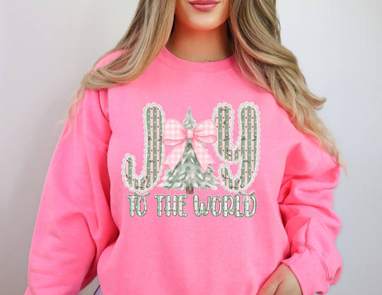 Person wearing a bright pink Joy to the World Crew sweatshirt featuring cacti and a Christmas tree design spelling JOY, showcasing festive style and comfort.
