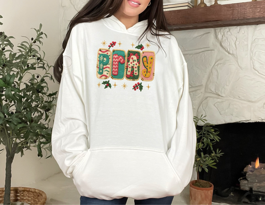 Person wearing a PLAY hoodie with festive graphics, featuring colorful knit-style letters and holly sprigs, perfect for cozy, stylish wear.