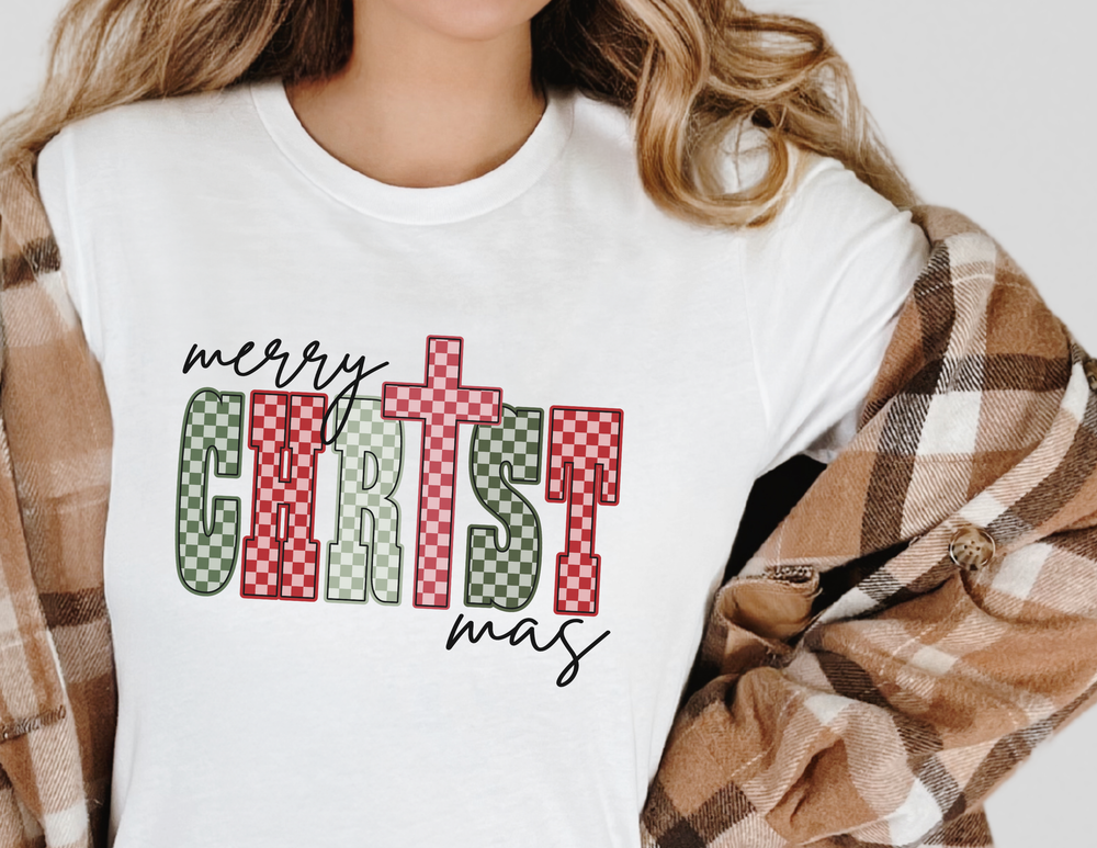 Person wearing a white Christmas Tee with merry CHRISTmas in green and red letters, paired with a tan plaid overshirt.