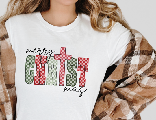 Person wearing a white Christmas Tee with merry CHRISTmas in green and red letters, paired with a tan plaid overshirt.