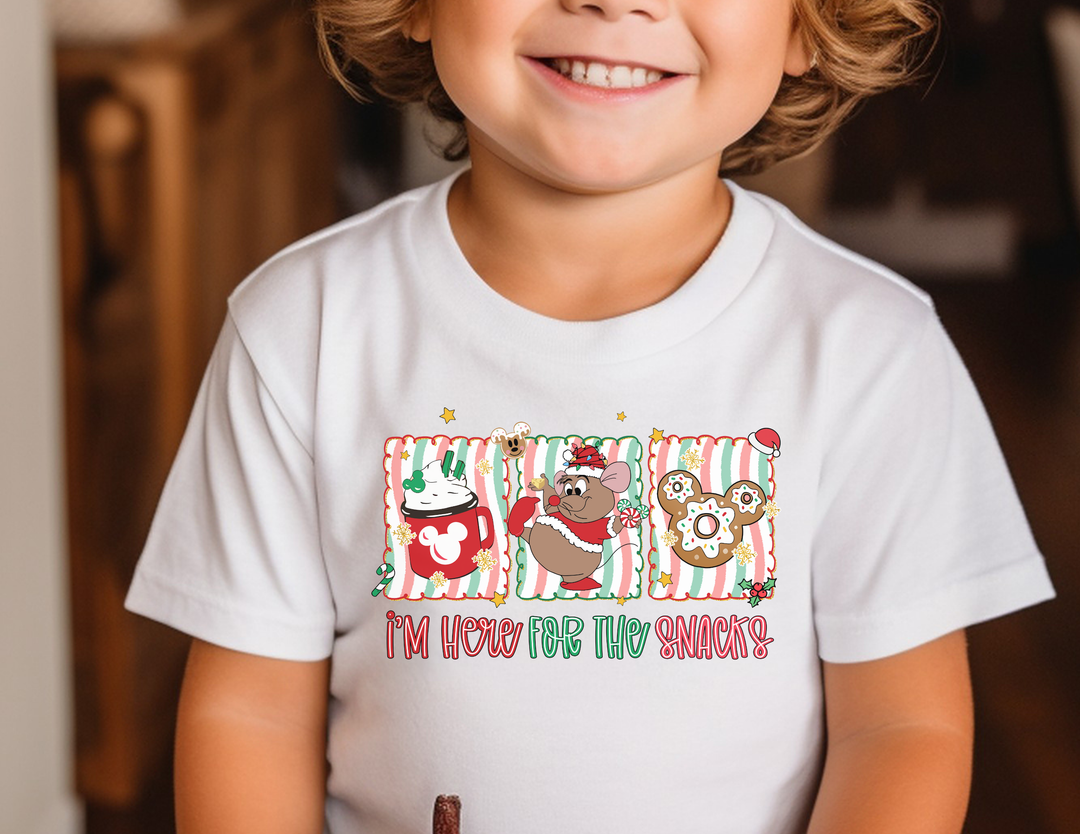 Child wearing Here for the Snacks Kids Tee featuring festive cartoon panels with hot chocolate, cheerful mouse, and Mickey-shaped doughnut. Perfect for everyday use.