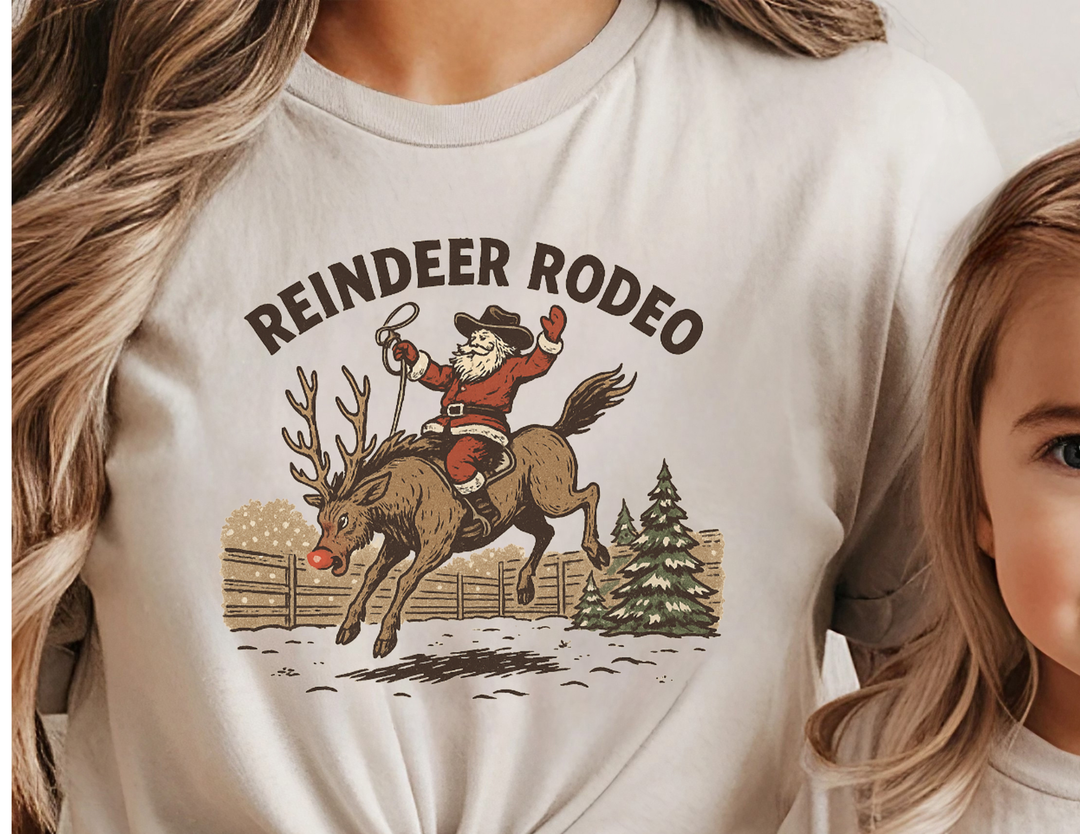Reindeer Rodeo Tee: Vintage Christmas design with Santa as a cowboy on a reindeer. Soft, unisex fit, ideal for festive, western-themed styling.