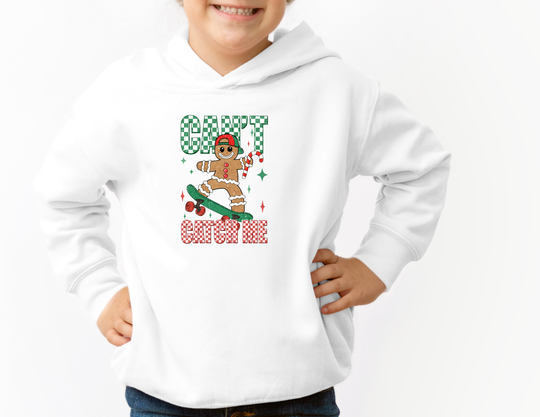 Child in Can't Catch Me Youth Hoodie featuring a gingerbread man on a skateboard, holding a candy cane. The hoodie offers a soft fleece feel with a front pocket.