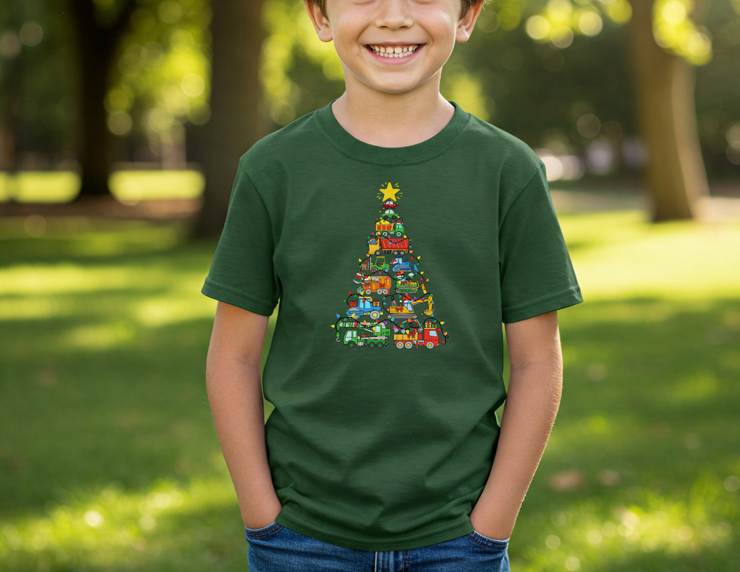 Young boy wearing a Christmas Truck Kids Tee with a whimsical vehicle-themed Christmas tree graphic, smiling in a sunny park setting.