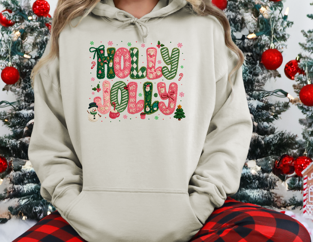 Person wearing HOLLY JOLLY hoodie with festive knit-pattern motifs, seated by a Christmas tree, showcasing cozy, stylish holiday-themed design.