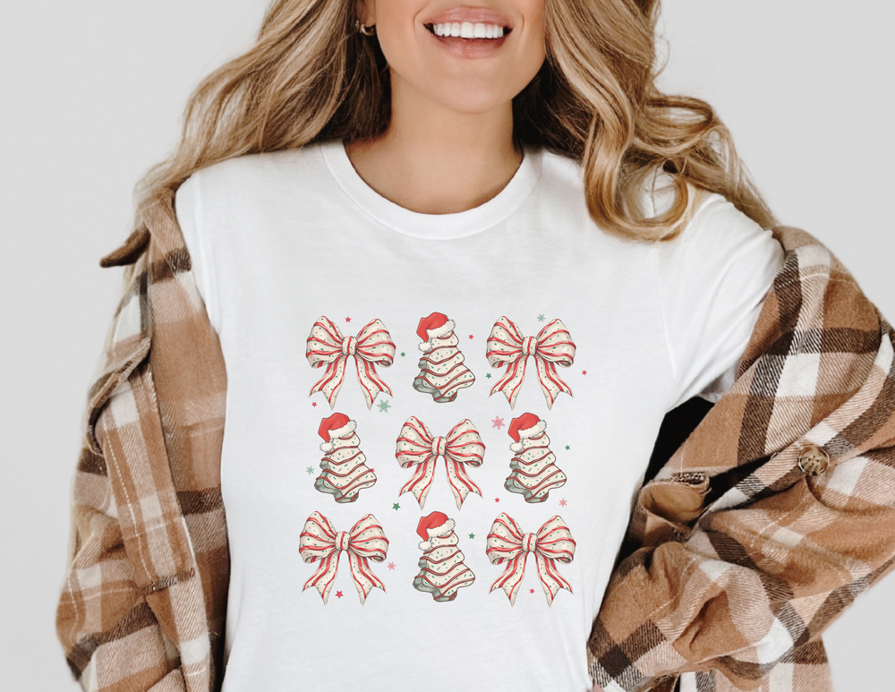 Person wearing Faith Family Designs' Cookies and Bows Tee, featuring a 3x3 grid of Christmas-themed illustrations, beneath a light-brown plaid shacket, smiling subtly.