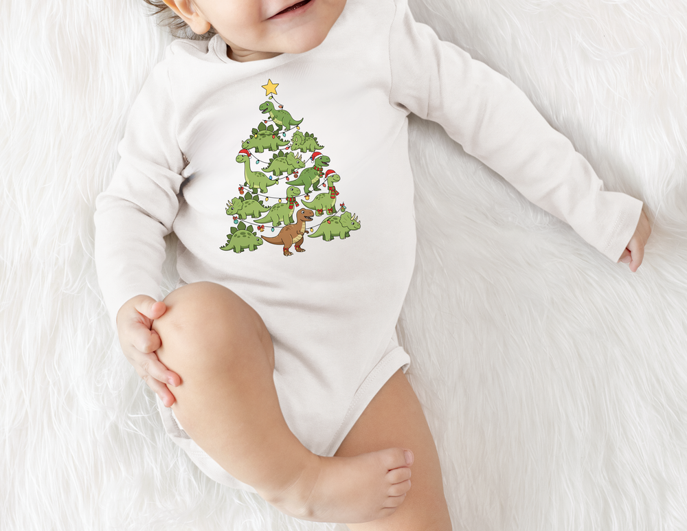 Baby wearing a Baby Dino Tree Onesie on a white furry surface, featuring cartoon dinosaurs as a Christmas tree with lights, hats, and a star.