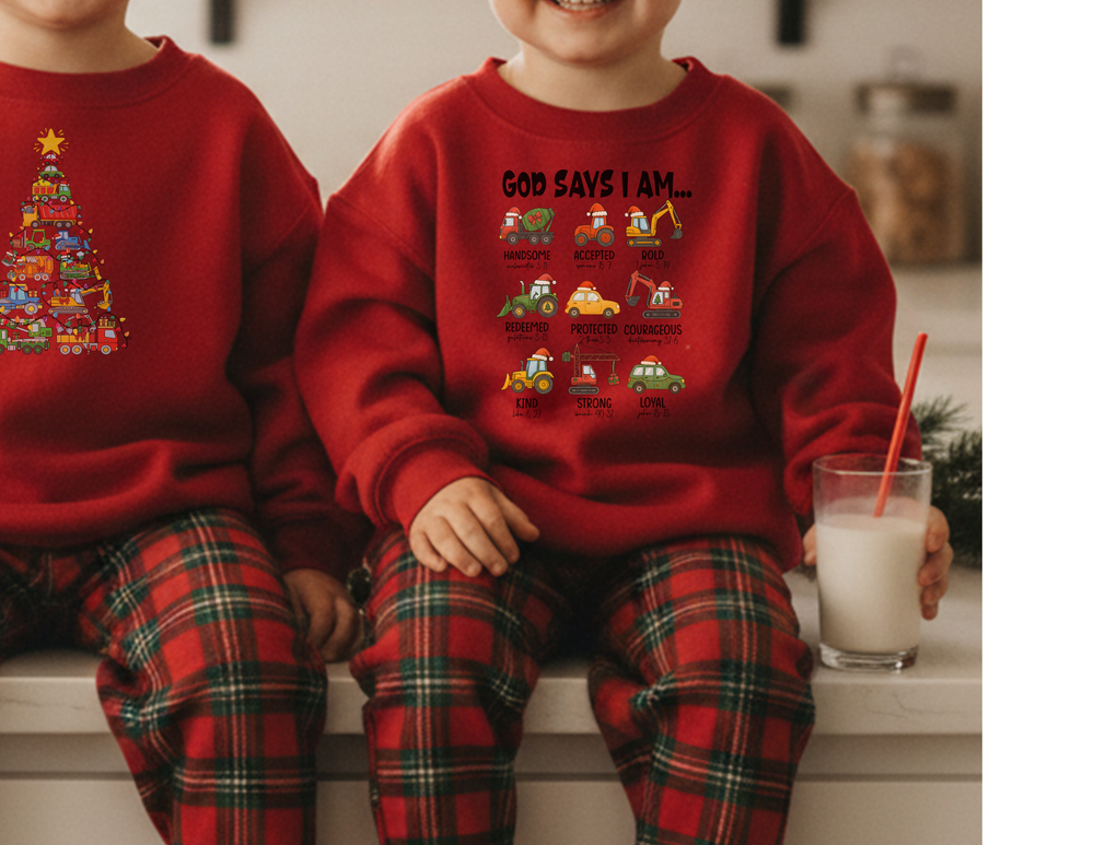 Two children in matching red God Says Christmas Truck sweatshirts and plaid pajama pants sit on a counter, one holding a milk glass with a straw.