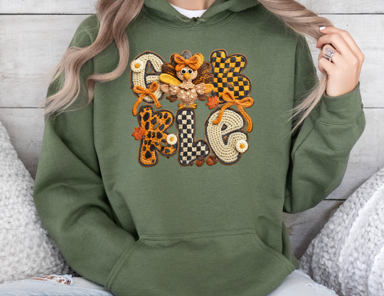 Gobble Hoodie with crochet-style GOBBLE applique, featuring patterns, bows, daisies, leaves, and a cartoon turkey. Modeled by a person, showcasing hoodie fit.