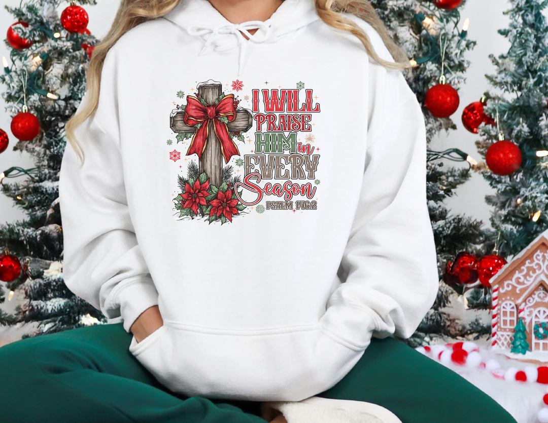 Person wears a Praise Him in Every Season hoodie featuring a cross with a red bow, surrounded by poinsettias and snowflakes, embodying festive faith-based design.