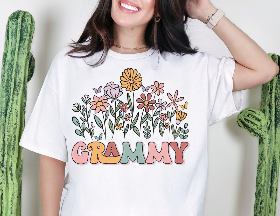 Person wearing Grammy Flower Tee with pastel flowers and butterflies, smiling in front of cactus plants. Classic unisex fit, soft cotton, perfect for everyday wear.