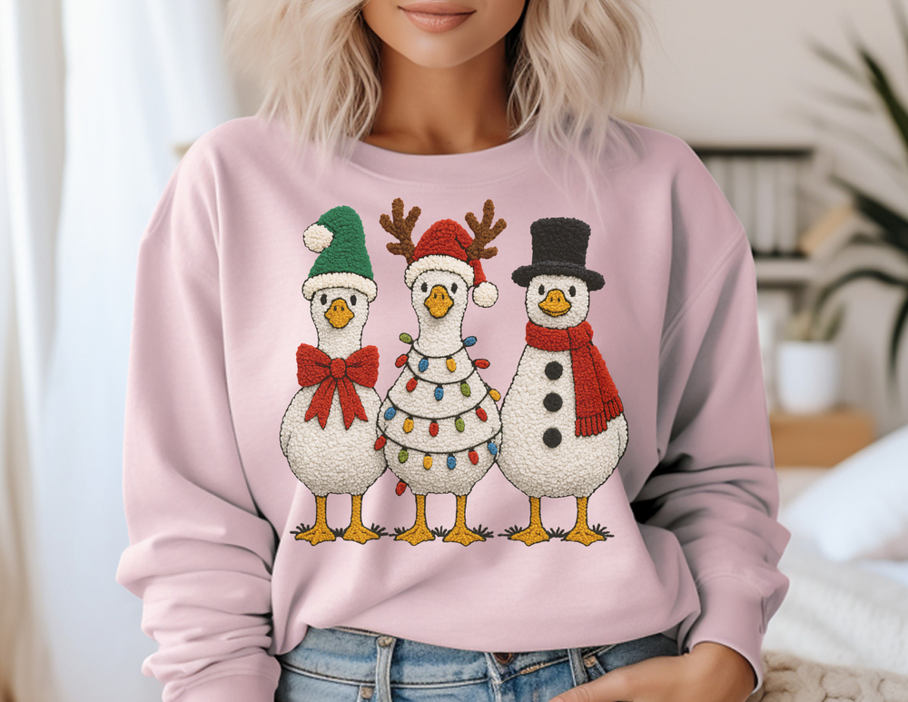 Light pink sweatshirt featuring cartoon-style geese in holiday costumes, paired with blue jeans, embodying festive charm and comfort for a cozy winter look.
