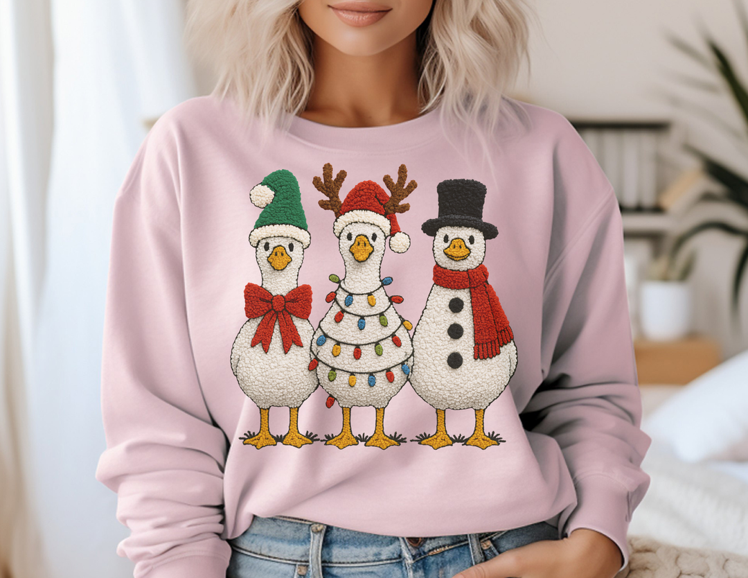 Light pink sweatshirt featuring cartoon-style geese in holiday costumes, paired with blue jeans, embodying festive charm and comfort for a cozy winter look.
