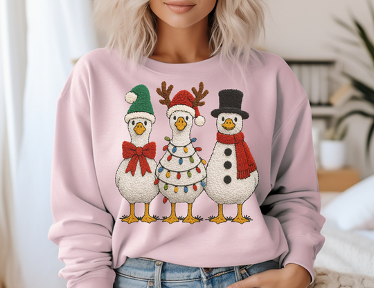 Light pink sweatshirt featuring cartoon-style geese in holiday costumes, paired with blue jeans, embodying festive charm and comfort for a cozy winter look.
