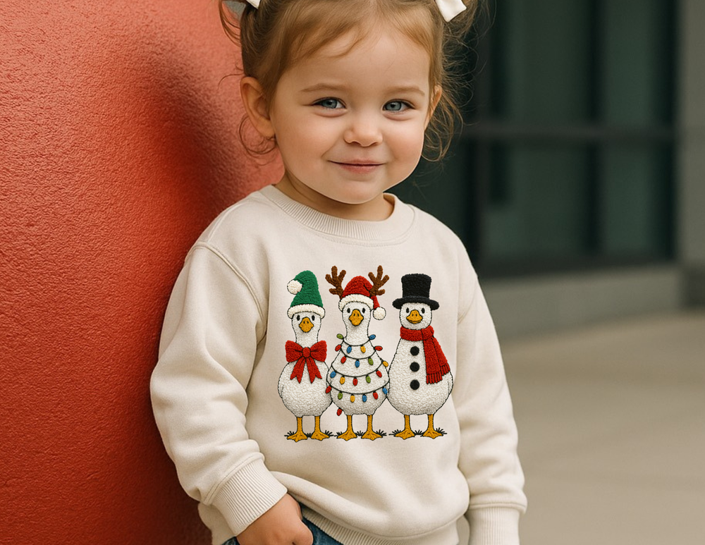 Toddler in festive Christmas Geese sweatshirt with cartoon birds in holiday attire, showcasing warmth and style from Faith Family Designs.