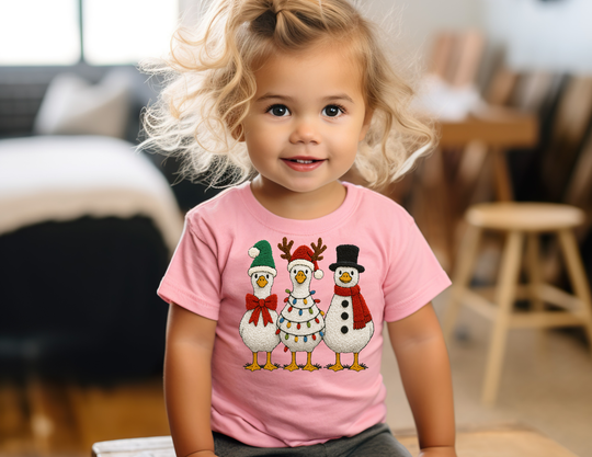 Toddler wearing Christmas Geese Baby Tee with festive birds, sitting indoors. The tee is soft, durable, and perfect for stylish first steps.