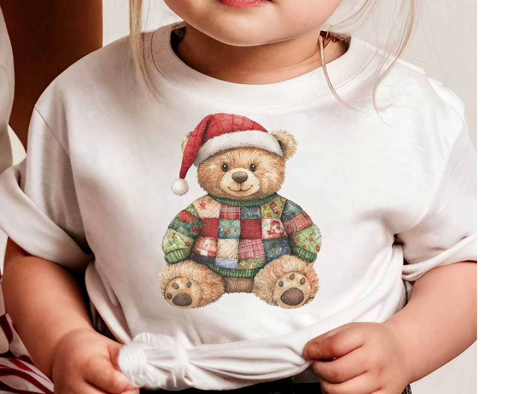 Child wearing Christmas Bear Baby Tee with festive teddy bear design, featuring a colorful patchwork sweater and Santa hat. Ideal for babies, made from soft, durable cotton.