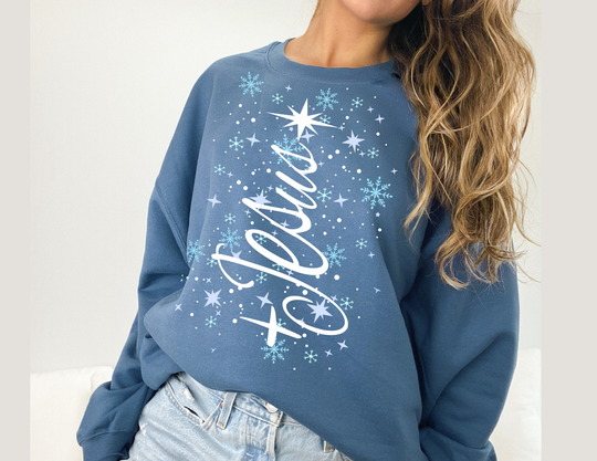 Person wearing a Jesus Tree Crew denim-blue sweatshirt with festive to you print, paired with light-wash jeans, showcasing a cozy, winter-themed design.