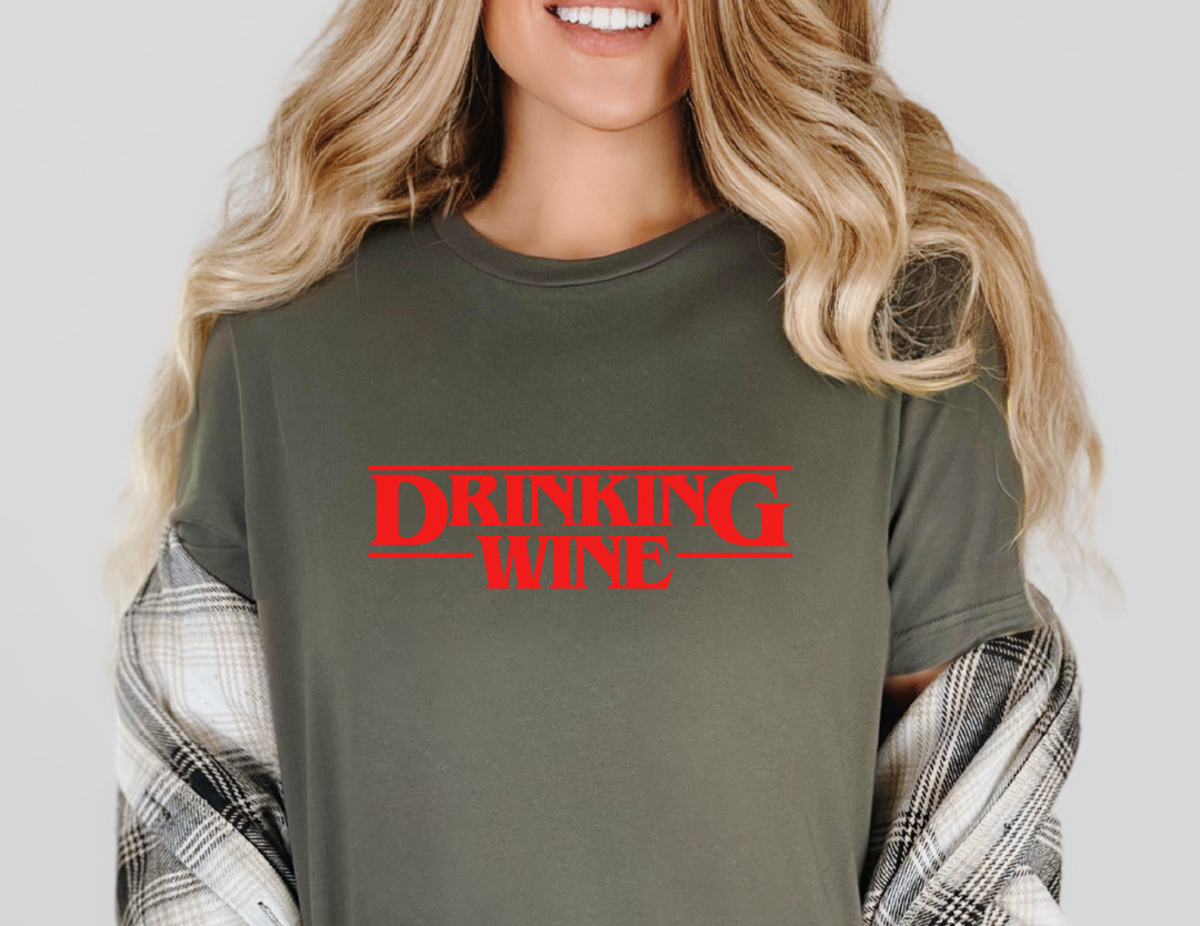 Woman wearing a DRINKING WINE graphic t-shirt, smiling at the camera. The relaxed-fit tee is soft-washed, 100% ring-spun cotton, ideal for casual wear.
