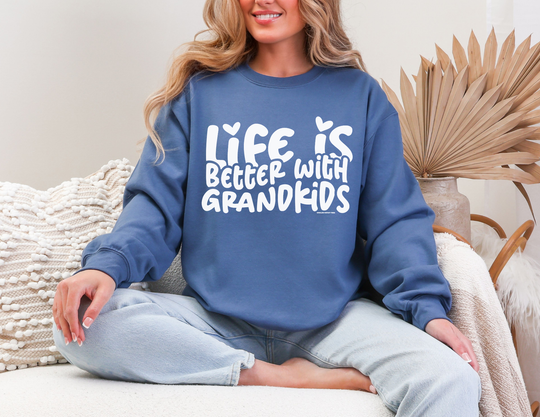 Person in a cozy living room wearing a Life is Better With Grandkids blue sweatshirt, showcasing comfort and style from Faith Family Designs.