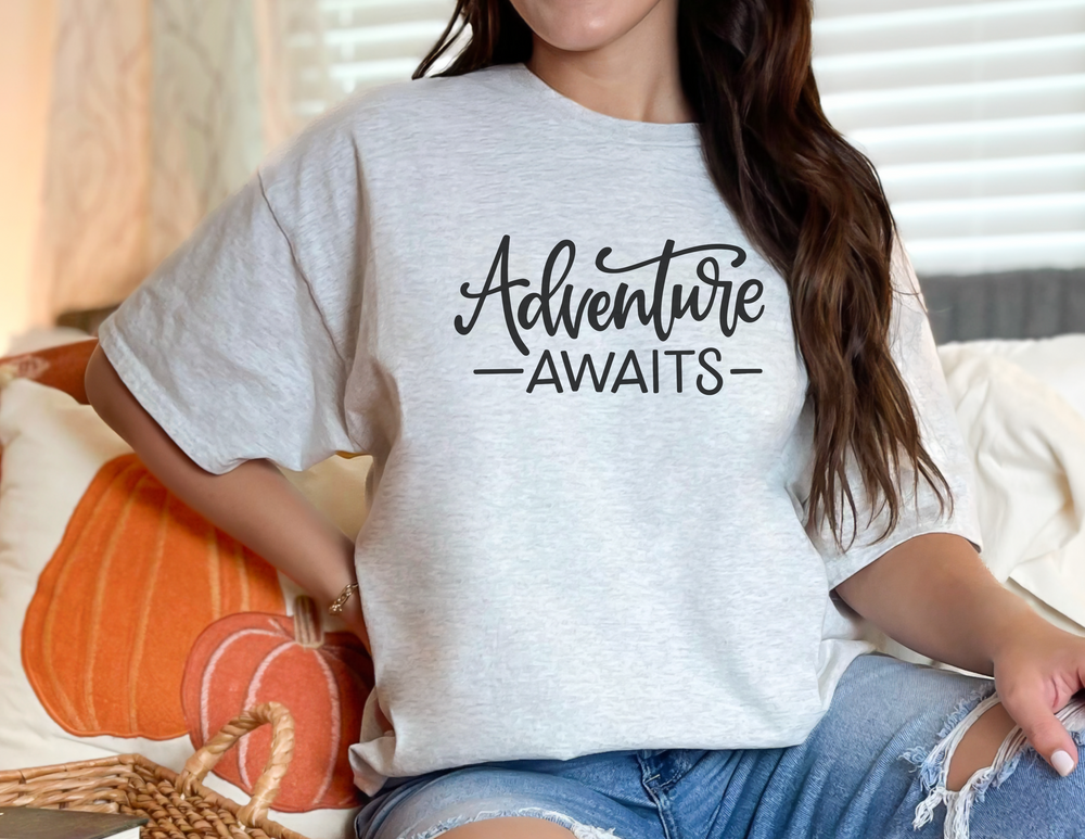 A premium Adventure Awaits Tee for men, featuring ribbed knit collar, roomy fit, and 100% combed, ring-spun cotton. Light and comfy, perfect for workouts or daily wear.
