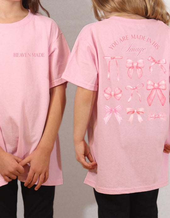 Two children in pastel-pink Heaven Sent Toddler T-shirt, featuring HEAVEN MADE front text and back print with bows and inspirational message.
