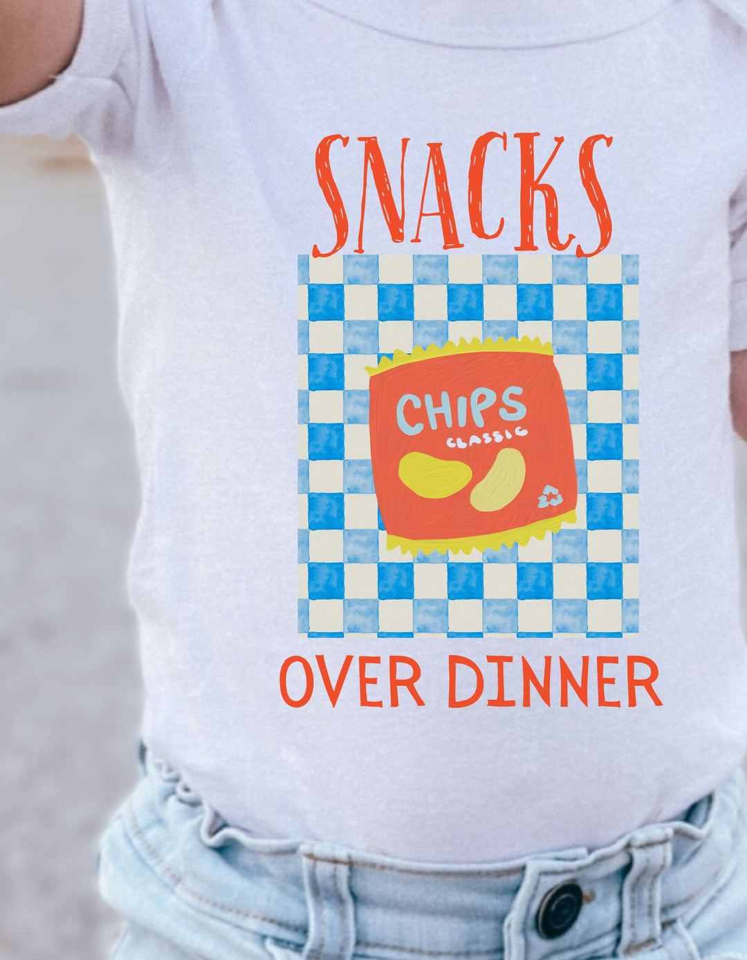 SNACKS Toddler T-shirt features bold graphics with SNACKS and OVER DINNER text, showcasing chips on a checkerboard design, offering style and comfort.